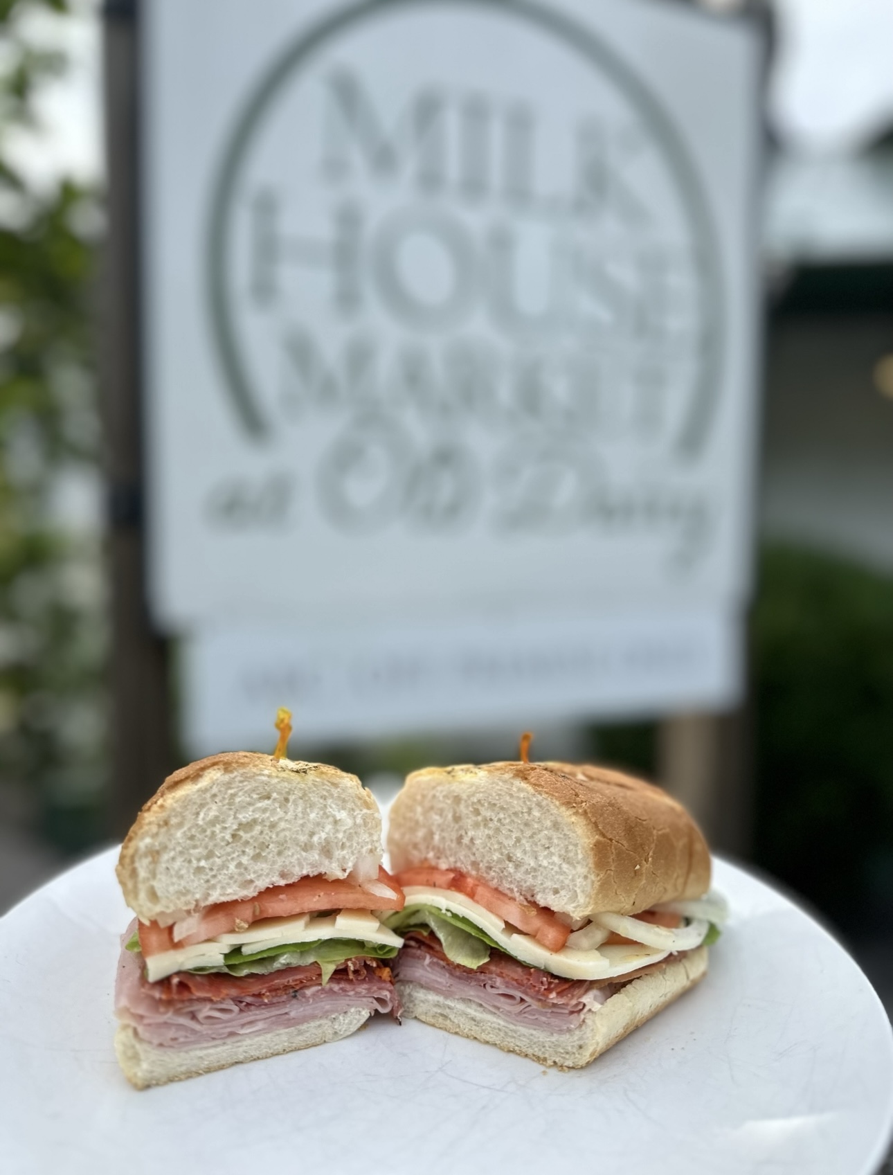 A freshly made market sandwich in front of the Milk House Market sign